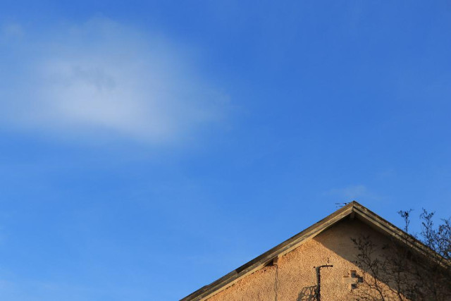 An image of a blue sky with a pale fluffy white cloud at the upper left and a yellow-ish top of a sunlit gable at the low right. 