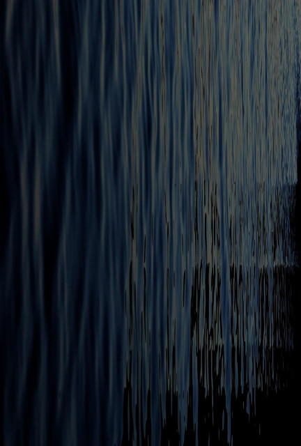 A tilted photo showing dark, vertical ripples shimmer across water with reflections fading from deep blue into black.