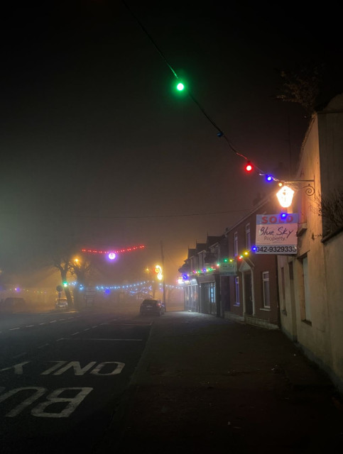 A foggy little village road lit up by multi coloured lights.