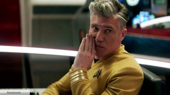 A screenshot from Star Trek Strange New Worlds featuring a profile of Captain Pike and his hair facing the left. Pike and hair are looking to the left, with Pike holding a hand in front of his face as if to speak an aside in the direction of the viewer.