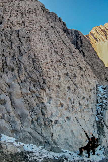 A photograph of two walkers at the base of the cliff gesturing towards the footprints with their walking sticks
