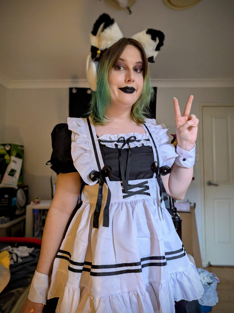 Revy wearing cat ears and a maid outfit dress
Black lipstick and eyeshadow.
She's doing a peace sign