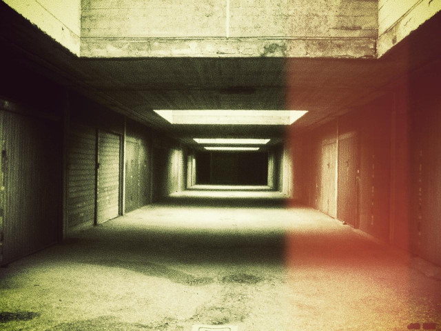 Dunkles Farbfoto einer unterirdischen Garage mit geschlossenen Garagentoren rechts und links und einem schwarzen Ende im Hintergrund. Rechts rötlich ein Lichteinfall.