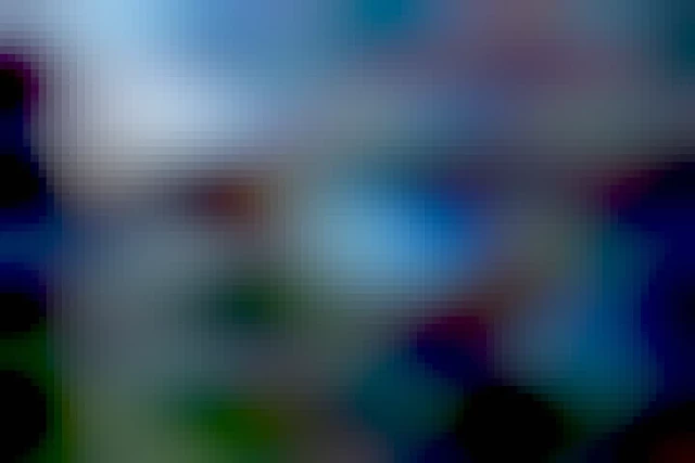 ein Riesenrad wurde aus der Höhe des zweiten Stocks in der Abenddämmerung in Bewegung fotografiert. durch eine verlängerte Bewegungszeit sind die bewegten Elemente und Lichter des Fahrgeschäfts verwischt. Damit es auf das Bild passt, wurde die Kamera schräg gestellt. Auf den ersten Blick sieht es daher so aus als würde es nach hinten umkippen