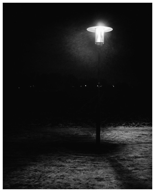 Eine Straßenlaterne steht in der Nacht ziemlich einsam neben einem Feld. Man sieht im wesentlichen den leuchtenden Lampenschirm und etwas erleuchteter Schnee unterhalb.