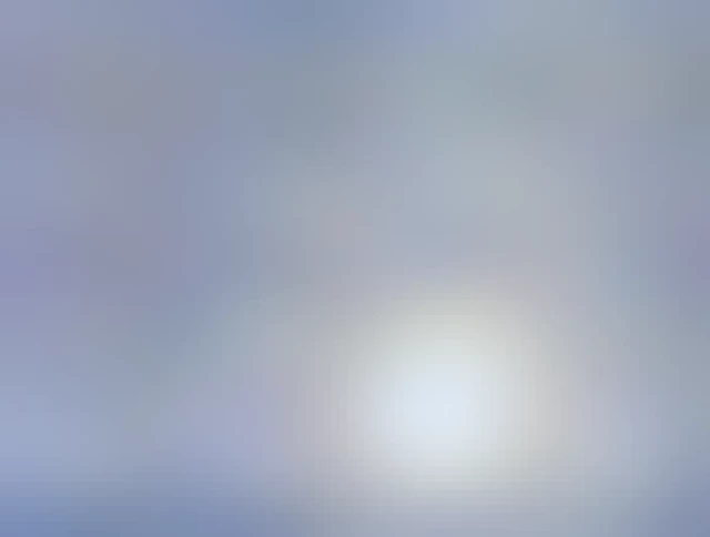 The sun is a big bright yellow ball of fire in a blue sky surrounded by glowing bits of blowing snow