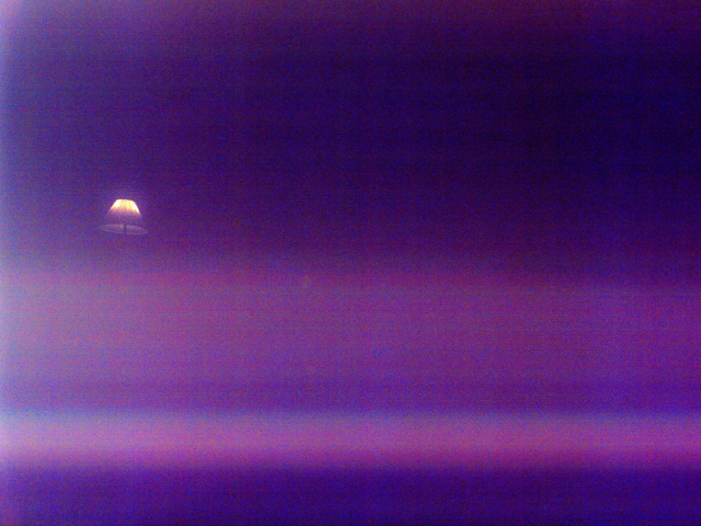 A graduated purple field with an unexpected lampshade, illuminated and floating, on the left side of the field. 