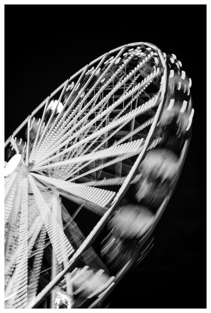 Riesenrad in schwarz-weiß, leicht schräg aufgenommen, mit Bewegungsunschärfe.