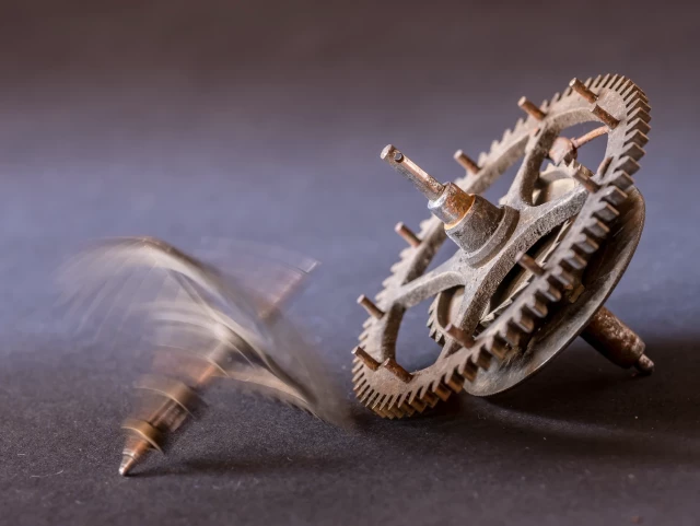 Zwei messingfarbene Uhrenzahnräder auf dunkelgrauem Untergrund - das eine liegt auf der Seite, das andere ist in der Drehbewegung eingefroren.