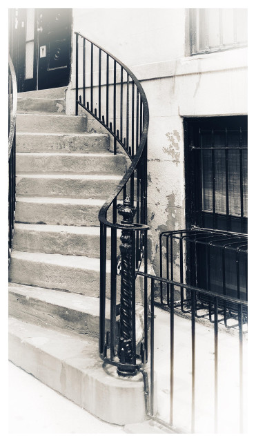 Black and white photo of an outdoor staircase leading down from a second-floor apartment door to the sidewalk. The stairs curve from the side of the landing, twisting 90 degrees to face the street. A black iron banister follows the curve of the stairs and curls around an ornate pole at the bottom, which has itself been molded with grooves that wind around it. Next to the stairs is the building’s flaking facade, in which is set a window with metal bars shaped to accommodate an air conditioning unit (but with no AC). Another low black railing separates the building from the sidewalk. The photo’s edges fade to white with a reverse vignette effect.