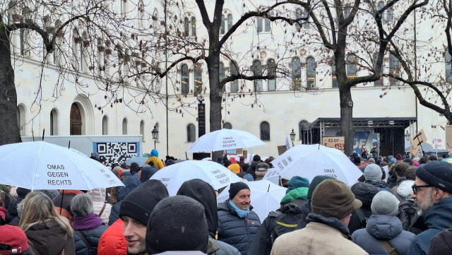 Bild von der Demo über Köpfe honweg. Omas gegen Rechts Regenschirme. Weißes Gebäude im Hintergrund, davor überdachte Bühne. Sieht nicht riesig aus.