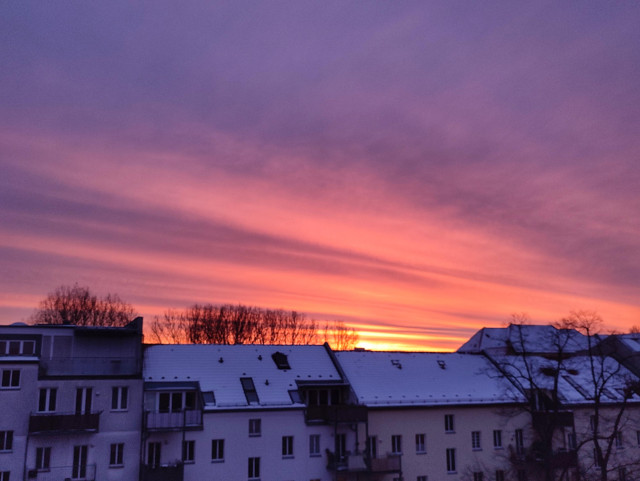 Orange-rosa Sonnenaufgang über verschneiten Dächern 