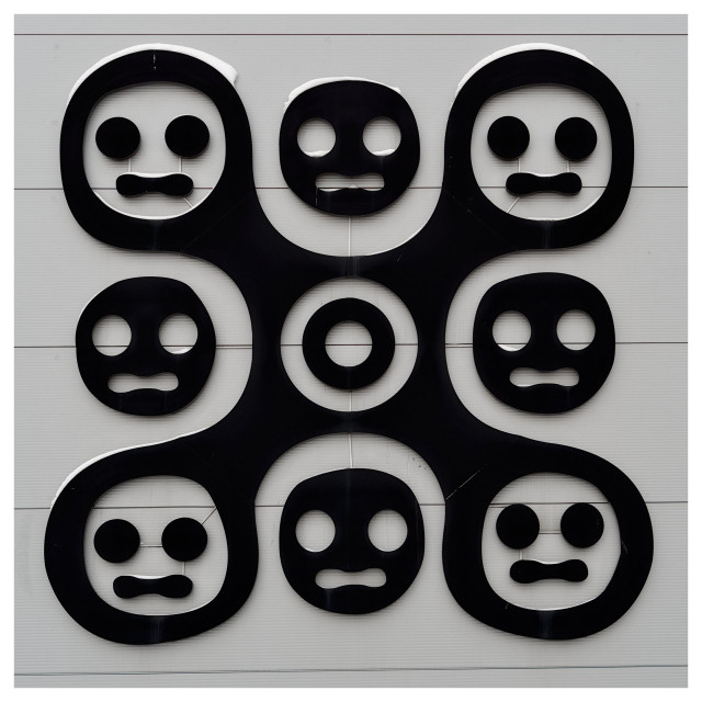 En fyrkantig monokrom bild på en symbol av stiliserade ansikten i en fyrkant med en ring i mitten.