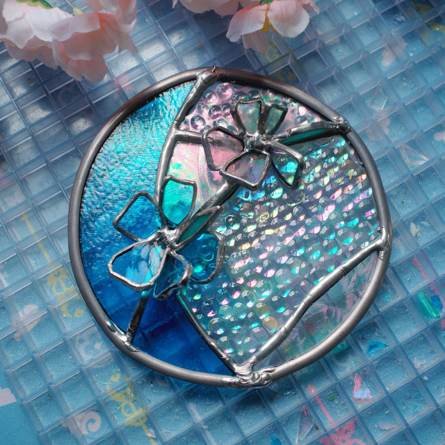 Stained glass piece with blue crescent moon and 3d flowers on top of iridescent glass.