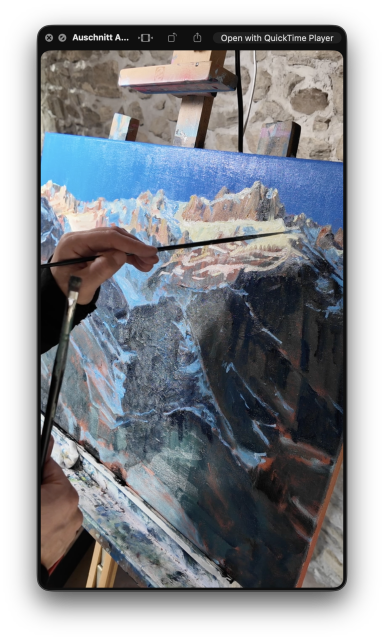 Die linke Hand der Künstlerin hält einen feinen Pinsel und malt gerade an einem mittelgrossen Bild (ca. 50 x 70 cm) In der anderen Hand hält sie einen dickeren Pinsel. Das Bild, welches gerade entsteht, ist von einem realistischen, felsigen, schneebedeckten Berggrat. Die letzten Sonnenstrahlen berühren eben noch die obersten Felsen und Schneeflächen und tauchen es in ein warmes, goldenes Licht. Der Himmel darüber ist tief blau. Die unteren 2/3 des Berges liegen bereits im dunklen Schatten. Das Bild drückt eine tiefe Ruhe aus.