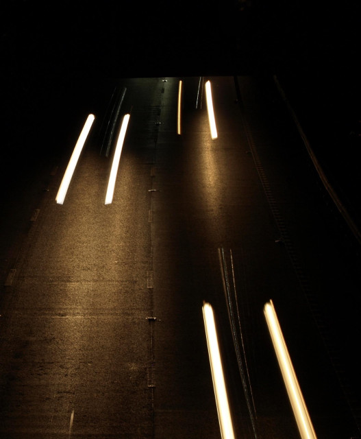 Looking down on a motorway where the shutter speed has made the cars invisible but short streaks of headlights come out of nowhere. 