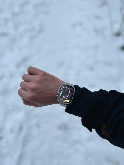 A person's left arm and wrist wearing a smartwatch, with a snowy landscape in the background.