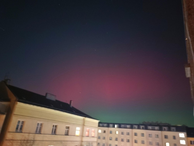 Rosa und grüne Polarlichter über Häuserdächern