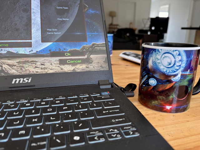 A laptop computer with the starcraft start up screen. A mug with a protoss spacecraft on it. Jets flaring. 