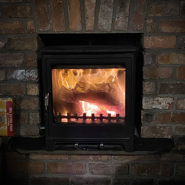 A wood burning stove set in a brick wall with a fire blazing.