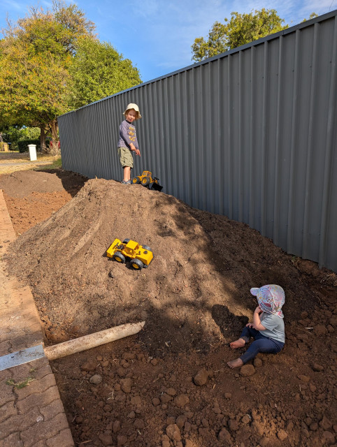 Before: a photo of our verge, with a big pile of soil. 2 kids are playing with toy diggers in the dirt