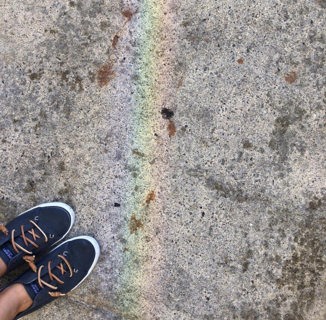 Navy shoes in the lower left corner, rainbow on a sidewalk takes up most of the frame 