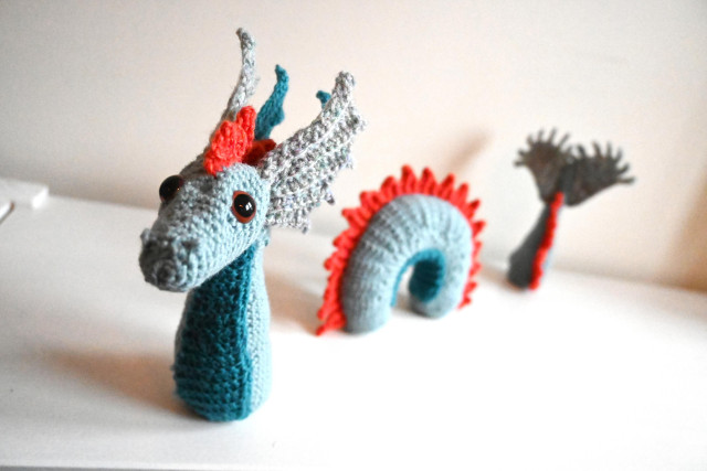 Foto av ein hekla sjøorm i tre delar: Start, midt og slutt. Oppstillinga gir ein illusjon av at sjøromen ligg halvveges nedi vatnet. Sjøormen har blågrøn kropp og raude skjel langs ryggen.