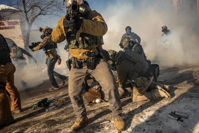 A chaotic scene depicting law enforcement officers in tactical gear during a confrontation. Smoke fills the air, and some officers are seen engaging with individuals on the ground. Various equipment and debris are scattered across the street.

David Guttenfelder/The New York Times