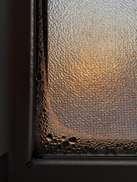 Condensation on the edge of a privacy window on a cold day. The rising sun is coloring the water drops a warm peachy color. 
