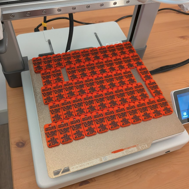 A photo of a 3D printer showing dozens of printed whistles labeled "Anti-ICE Whistle. ICE near: 3 short blasts. ICE Arrest: long blasts."