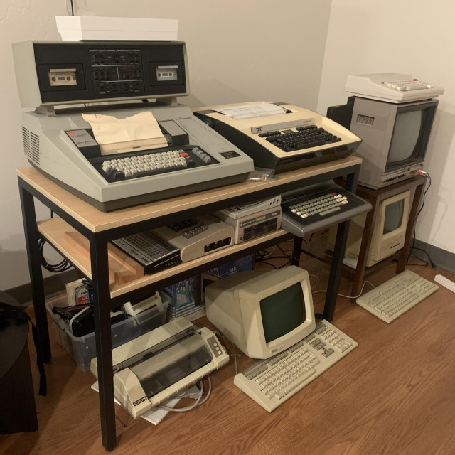 Top to bottom, left to right:
- PiDP-11, TI Silent 700 Model 733 ASR, Teletype Model 43
- TRS-80 Pocket Computer 2, Commodore 64, Commodore 1541 floppy drive, AlphaSmart Pro, Color Computer 1, (hidden) Color Computer 2
- C.ITOH Prowriter Jr., VT220, accessories
- Color Computer 3, Commodore 1702 video monitor, Macintosh SE