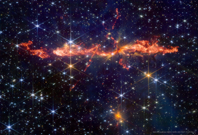 An image of a young protostellar outflow called HH288 in space, as seen with JWST. Much of the background is dark black and blue, with many stars sprinkled across with different colours and brightnesses, many showing the classic eight-pointed shape that comes from the JWST optics. The Dragon Jet itself is a swath of red, orange, and yellow emission spread horizontally across the image, with at least two crossing flows. The main flow resembles a Chinese dragon, hence the name. 