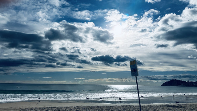 Unedited photo of beach in Benidorm from vacation including a beach pole and blue white sky