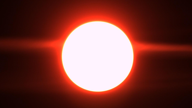 A bright, glowing white circle with a red-orange glow around it, resembling a solar eclipse or the sun.