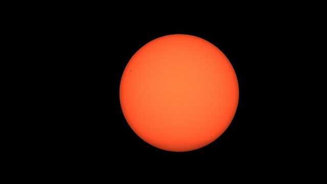 A bright, orange sun with a smooth surface against a black sky,