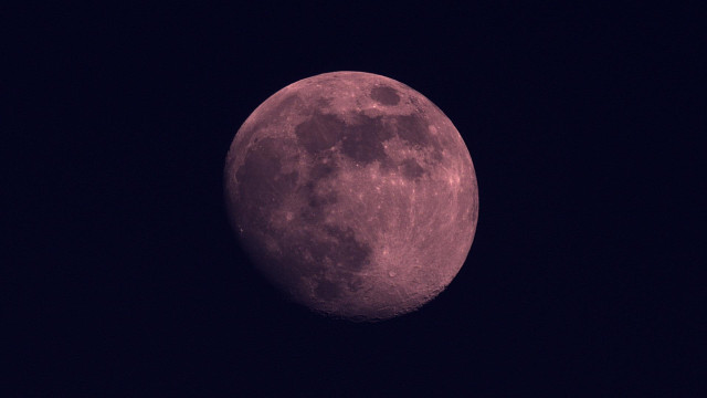 A pinkish, full moon against a dark night sky, showing detailed surface features with craters and maria.