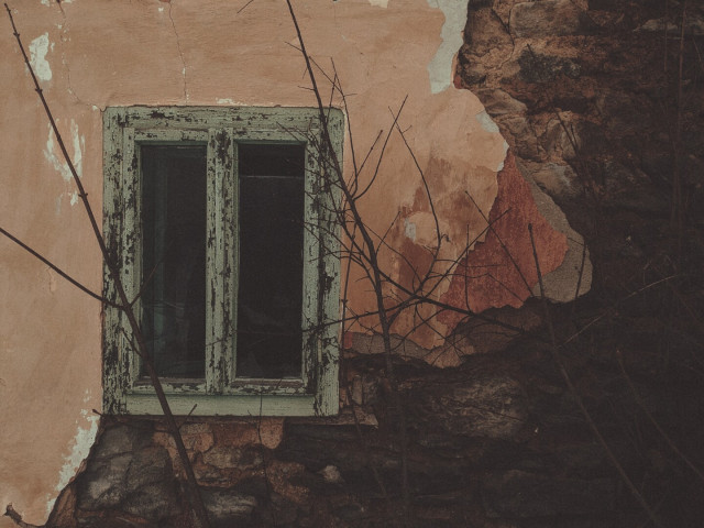 A green wooden window in the crumbling wall of an old building.