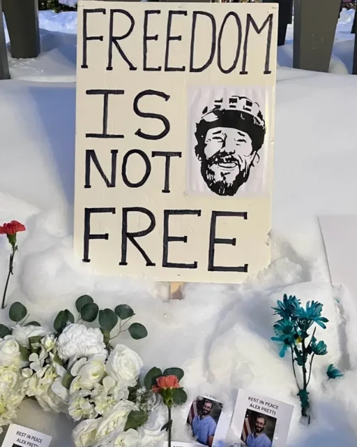 A placard laid in the snow sows a pen and ink portrait of Alex, with the words FREEDOM IS NOT FREE, surrounded by flowers.
