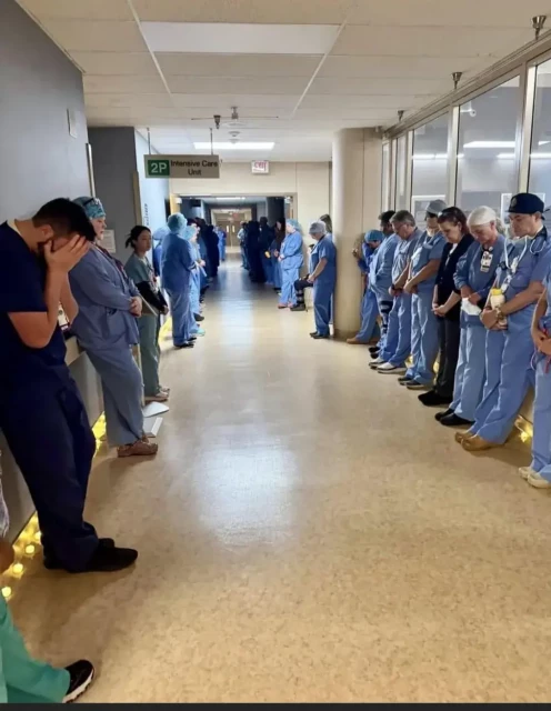 Alex's colleagues line the corridor with heads bowed.  Some are holdinng their heads in their hands.