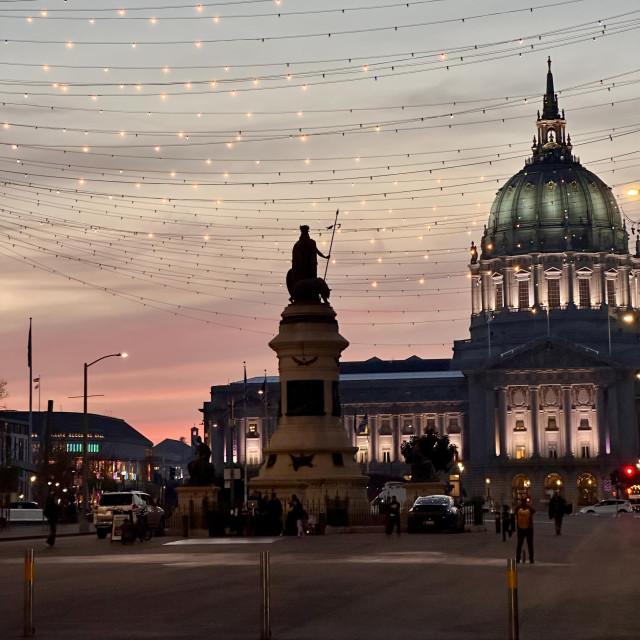 A photo of San Francisco city hall with a pinkish sunset in the background and street lights 