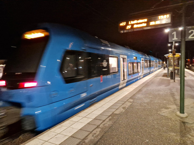 Ett tåg på Roslagsbanan i rörelse sedd från en perrong, på kvällen.