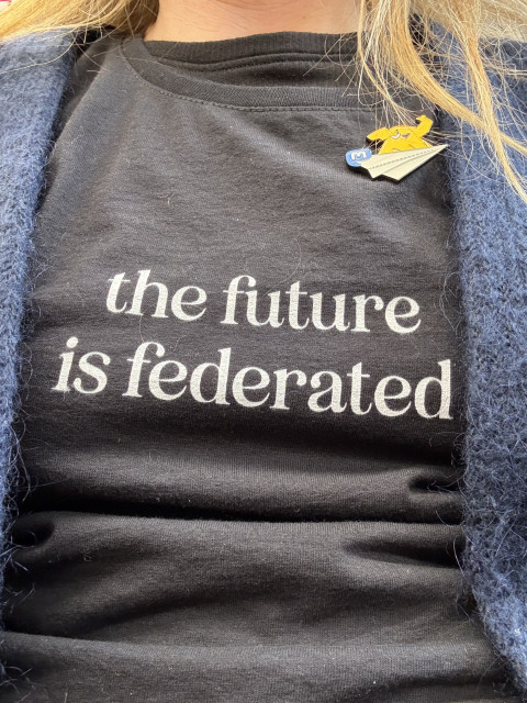 Picture of the t-shirt I’m wearing todat. A black one with the text in white ‘the future is federated’. Above that a Mastodon pin with a flying mastodon on a paper plane.