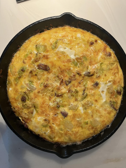 An eggy yellow, green and white-flecked, nicely browned omelette in a cast iron skillet.