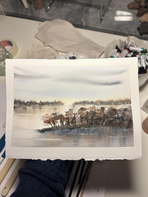 En akvarellskiss på ett papper i landskapsformat av ett höst eller vinterlandskap med träd som speglar sig i vatten.