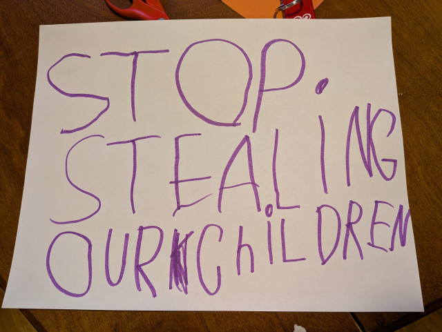 Paper sign written by a child that says "Stop stealing our children" 
