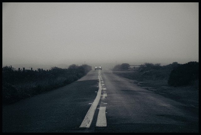 A dark scene on a very foggy morning at Point Reyes National Park. It's a picture of a small passenger car, with headlights on, driving in the middle of an asphalt, two lane road. The car somewhat straddles the lane marker in the center of the road, carefully avoiding the road edges because you never know when a deadly animal might leap out and attack. 

Okay I made that last part up. But what I didn't make up is the car is coming out of a heavy bank of fog and heading straight for me. Also, there are no trees... just small native bushes and weeds on either side of the road - the typical chaparral of this portion of the California coast.

Monochromey - slightly bluish and brownish dual tone but otherwise colorless - with limited dynamic range. There are no bright spots except for the car headlights. The sun would not come out for another 3 hours.