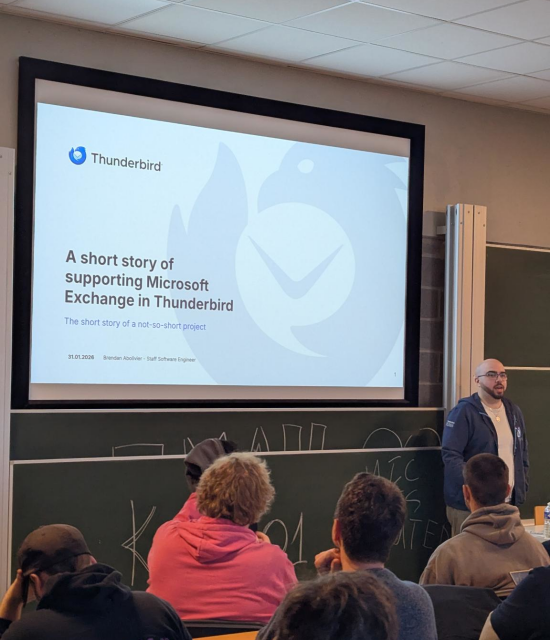 A photo of me talking to an audience, with a title slide projected on the wall that reads "A short story of supporting Microsoft Exchange in Thunderbird".