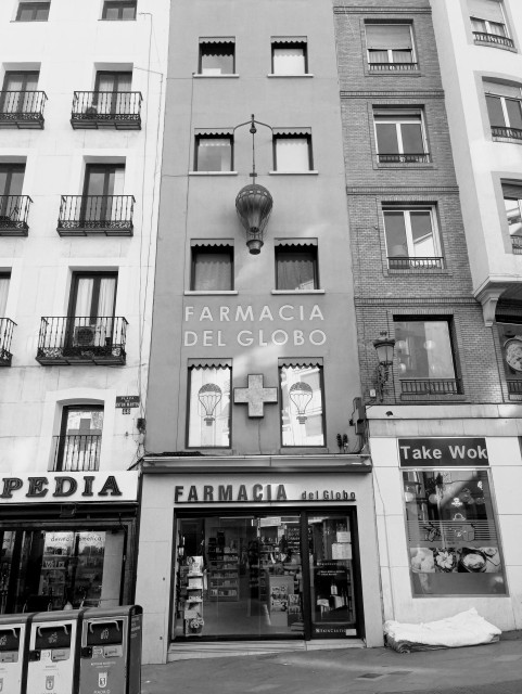 My black and white photo of a building with a pharmacy at the bottom and 3 stories of windows above in the middle is a detailed replica of an old style hit air balloon.