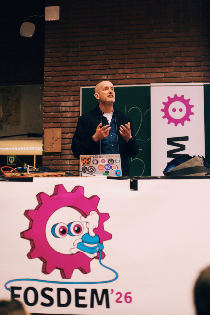 a photo of Björn Staschen on stage at FOSDEM, standing behind the podium