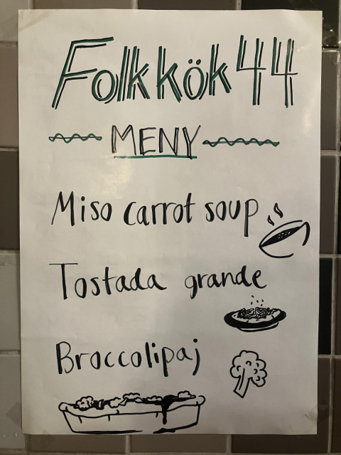 ​A hand-drawn menu on white paper titled "Folkkök 44 MENY". It lists three items accompanied by simple black ink illustrations: Miso carrot soup, Tostada grande, and Broccolipaj (broccoli pie).
